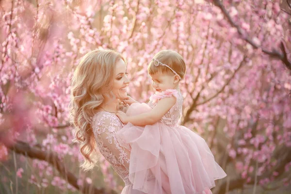 Porträtt av unga vackra mamma med hennes lilla tjej. Närbild av fortfarande av kärleksfull familj. Attraktiv kvinna håller hennes barn i rosa blommor och ler — Stockfoto
