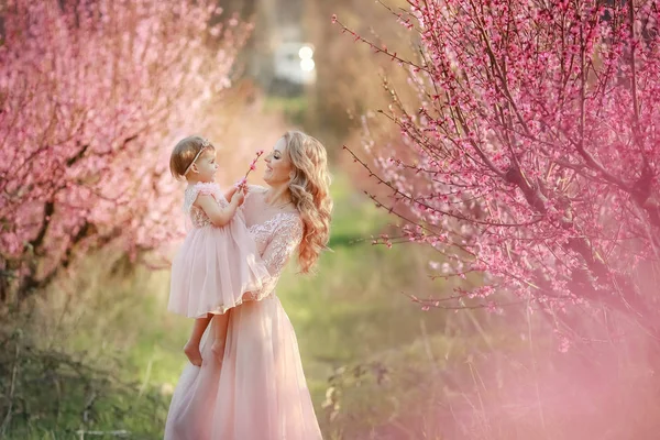 Maminka s malým dítětem v růžové zahradě se stromy květiny — Stock fotografie