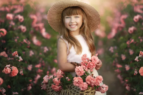 아름다운 긴 금발 머리를 가진 어린 소녀, 밝은 드레스와 그녀의 머리에 진짜 꽃화환을 입고, 차 장미의 정원에서 — 스톡 사진