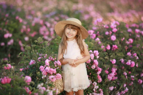Маленька дівчинка з красивим довгим світлим волоссям, одягнена в легке плаття і вінок з реальних квітів на голові, в саду чайної троянди — стокове фото