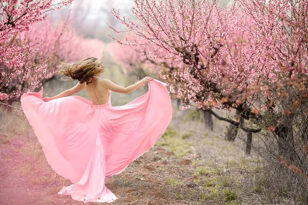 Een jonge prinses wandelingen in een bloeiende tuin. Meisje in een luxe roze jurk met een trein. Modieuze toning. — Stockfoto