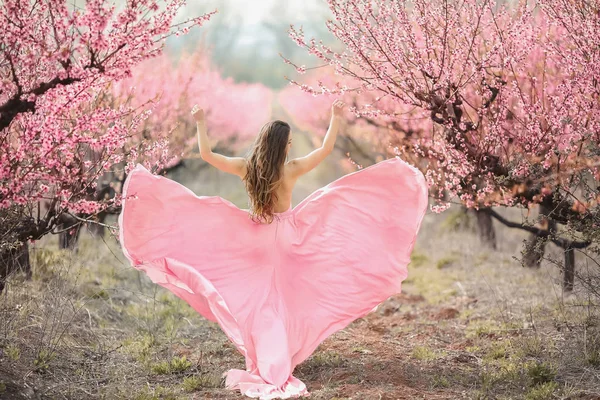 Een jonge prinses wandelingen in een bloeiende tuin. Meisje in een luxe roze jurk met een trein. Modieuze toning. — Stockfoto