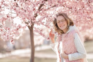 Kameraya bakan, sokakta poz veren, çiçek açan çiçeklerin yanında poz veren bir model. Kadın moda konsepti