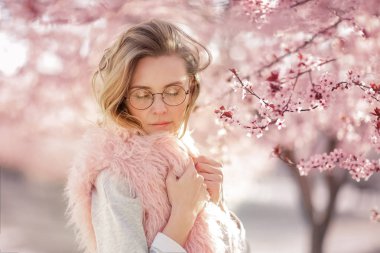 Kameraya bakan, sokakta poz veren, çiçek açan çiçeklerin yanında poz veren bir model. Kadın moda konsepti