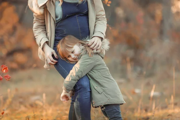 Беременная мать обнимает своего ребенка во время прогулки в парке — стоковое фото