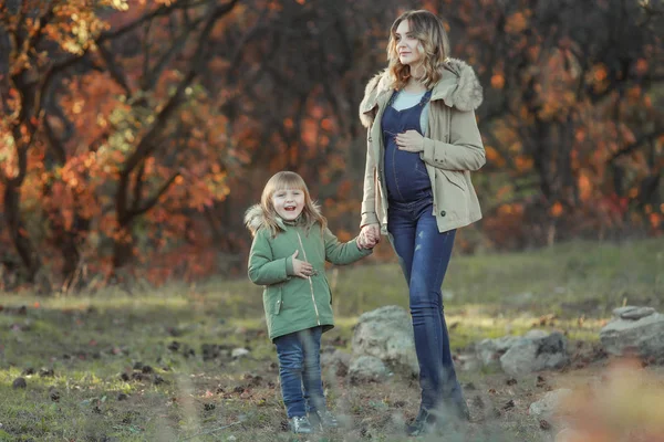 En pregnat mamma kramar sitt barn under promenad i parken — Stockfoto