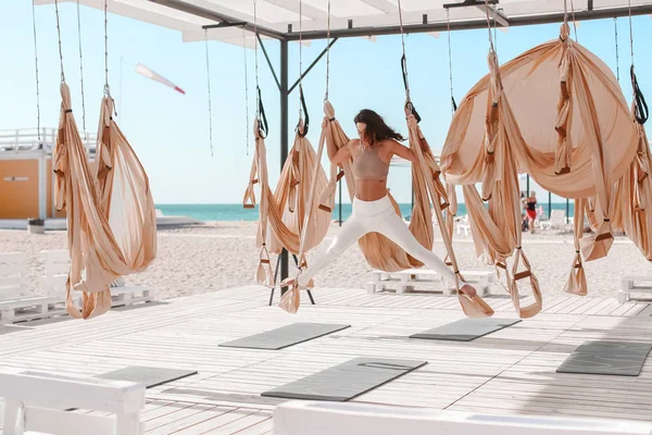 Uma bela mulher envolvida em ioga antigravidade ao ar livre junto ao mar na praia — Fotografia de Stock