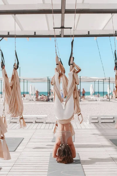 A Beautiful woman engaged in antigravity yoga outdoors by the sea on the beach — Stock Photo, Image