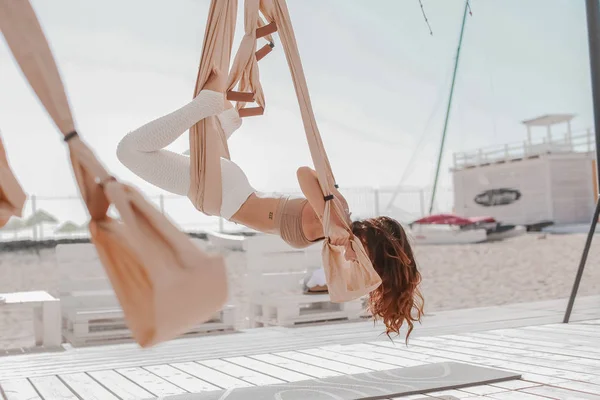 Een mooie vrouw die zich bezighoudt met antigravity yoga buitenshuis aan zee op het strand — Stockfoto