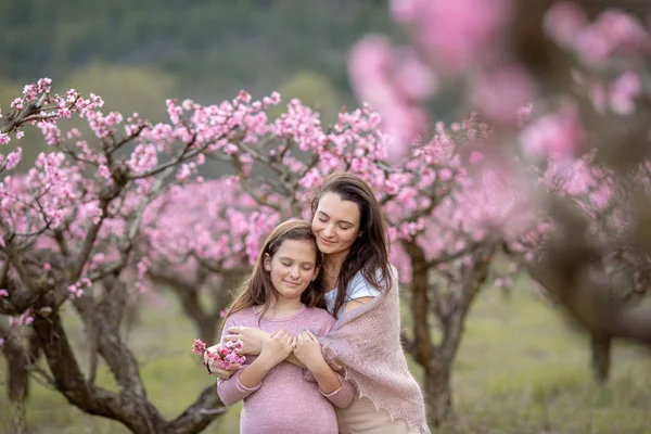 Jonge mooie moeder in het voorjaar, roze bloeiende boom op de achtergrond. — Stockfoto