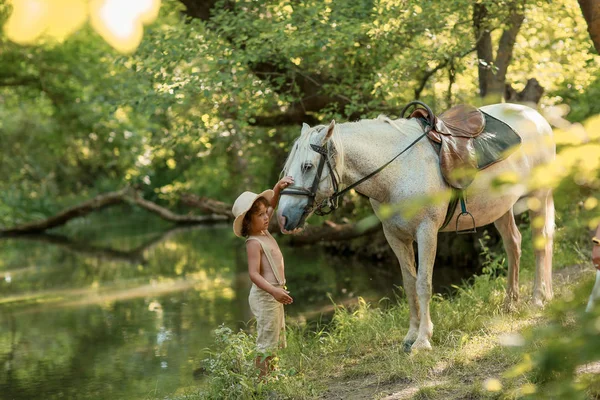 Liten pojke med lockigt hår klädd som Hobbit leker med hästen i sommar skogen — Stockfoto