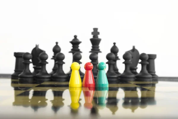 Group of colorful peons standing in front of a whole black chess army facing the risk of a confrontation.