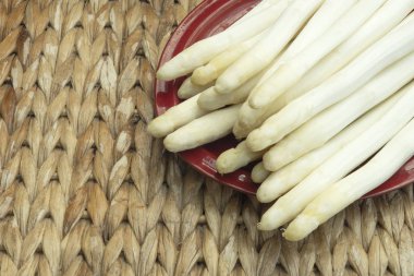 Arka planda hasır masa olan bir tabağa beyaz kuşkonmaz konmuş.