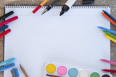Boya ve renk kalem, mum boyalar, suluboya, marker, kalem, kalemtıraş gibi yazmak için birkaç öğe ile boşaltmak ile ahşap bir masa üstünde şeritli defter