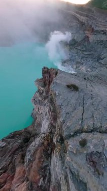 Sinematik FPV insansız hava aracı İjen volkanı krater gölü, Doğu Java 'ya çarpıcı sülfür buharı ve canlı turkuaz suyla uçuyor. Çiğ jeoloji, gerçeküstü manzara ve volkanik güzellik..