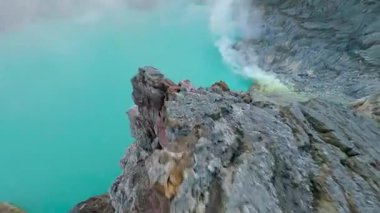 Sinematik FPV insansız hava aracı İjen volkanı krater gölü, Doğu Java 'ya çarpıcı sülfür buharı ve canlı turkuaz suyla uçuyor. Çiğ jeoloji, gerçeküstü manzara ve volkanik güzellik..