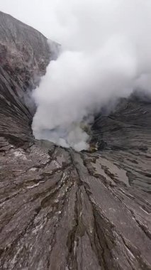 Doğu Java, Endonezya 'daki Bromo aktif volkanik kraterinin içinde FPV insansız hava aracı uçuşu. Kalderadan yoğun buhar yükseliyor. Doğa, seyahat ve macera temaları için mükemmel.