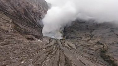 Doğu Java, Endonezya 'daki Bromo aktif volkanik kraterinin içinde FPV insansız hava aracı uçuşu. Kalderadan yoğun buhar yükseliyor. Doğa, seyahat ve macera temaları için mükemmel.