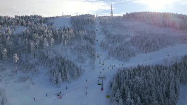 Kışın dağ eteklerinde kayak yapan ve teleferik kullanan insanların olduğu karlı bir yamaç manzarası. Seyahat, turizm, kış sporları, yaşam tarzı ve tatil macerası temaları için mükemmel..