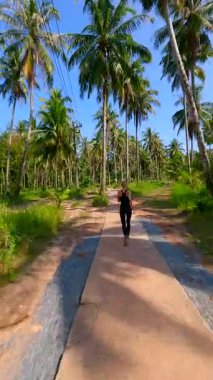 Güneşli bir günde çekilen, tropik palmiye ormanlarında koşan sağlıklı bir kadının sinematik FPV görüntüsü. Fitness, seyahat, refah ve aktif yaşam tarzı temaları için ideal.