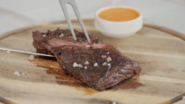 El hombre en el restaurante con un cuchillo corta filete de carne de mármol, a la parrilla. Sirviendo en una mesa de madera. Carne de res cocinando en una cocina. Carne fresca, deliciosa, picante y jugosa — Vídeos de Stock