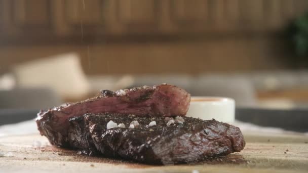 Sazonar con pimienta y sal. Filete a la parrilla en la parrilla. Carne de res cocinando en una cocina. Carne fresca, deliciosa, picante y jugosa — Vídeo de stock