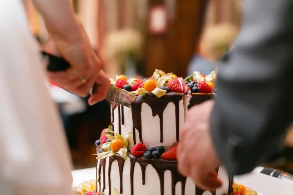 Bolo de casamento com bagas na mesa de madeira. Noiva e noivo cortam bolo doce no banquete no restaurante . — Fotografia de Stock