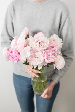 Sevimli ve güzel şakayık çiçekleri kadın elinde... çok katmanlı yaprakları. Soluk pembe peonies çiçekler açık gri renkli demet.