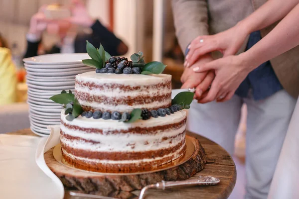 Bolo de casamento com bagas na mesa de madeira. Noiva e noivo cortam bolo doce no banquete no restaurante . — Fotografia de Stock