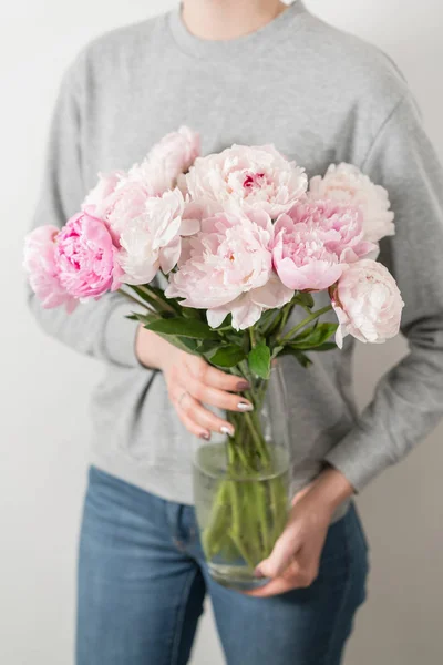 Flores de peônia bonito e adorável em mãos de mulheres.. muitas pétalas em camadas. Bunch peônias rosa pálidas flores luz fundo cinza . — Fotografia de Stock