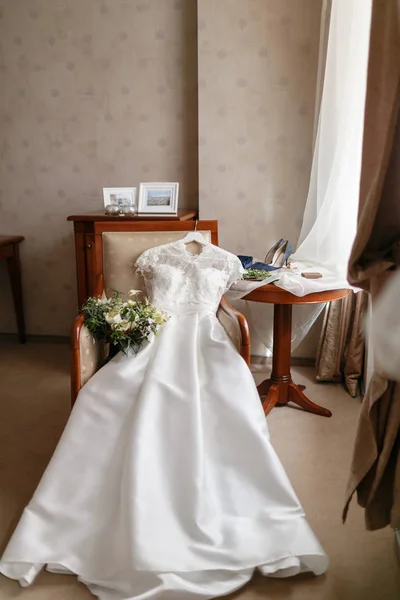 Белое свадебное платье с кружевами, лежащими на стуле. букет разных цветов. Современная свадебная компания с цветком мака и чертополохом. аксессуары для невесты на столе — стоковое фото