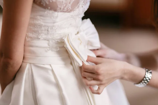 Одежда свадебного платья. Подружка невесты обвязывает бант на белом платье. Невеста ждет — стоковое фото