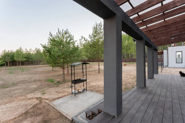 Vista laterale di una veranda aperta di fronte a un moderno cottage forestale. Pineta giovane foresta sotto i raggi del tramonto sullo sfondo . — Foto Stock