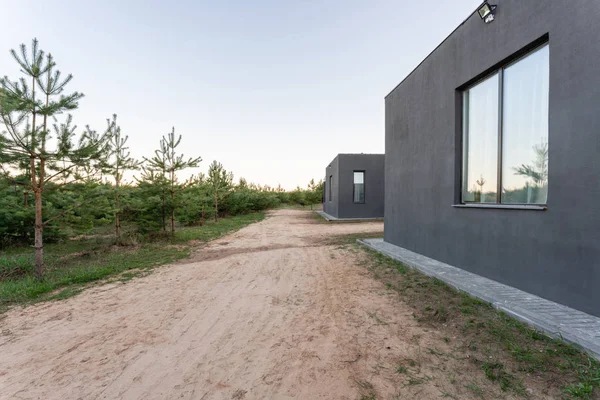 Vista laterale di una veranda aperta di fronte a un moderno cottage forestale. Pineta giovane foresta sotto i raggi del tramonto sullo sfondo . — Foto Stock