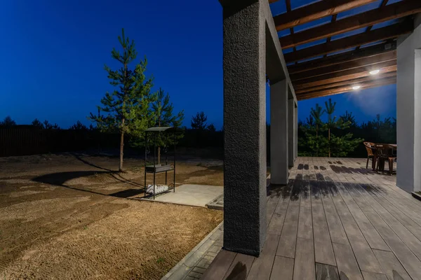 Vista laterale di una veranda aperta di fronte a un moderno cottage forestale. Pineta giovane foresta sotto i raggi del tramonto sullo sfondo . — Foto Stock