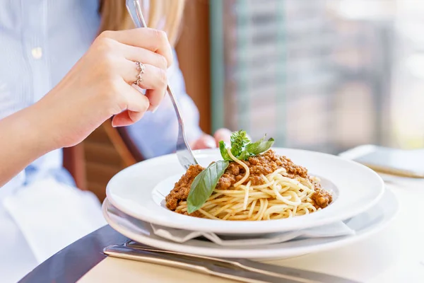 Młoda kobieta szczęśliwa, siedząc przy stoliku w kawiarni i delektować posiłkiem. Głodny kobieta jedzenie smaczne makarony. Danie Spaghetti Bolognese — Zdjęcie stockowe