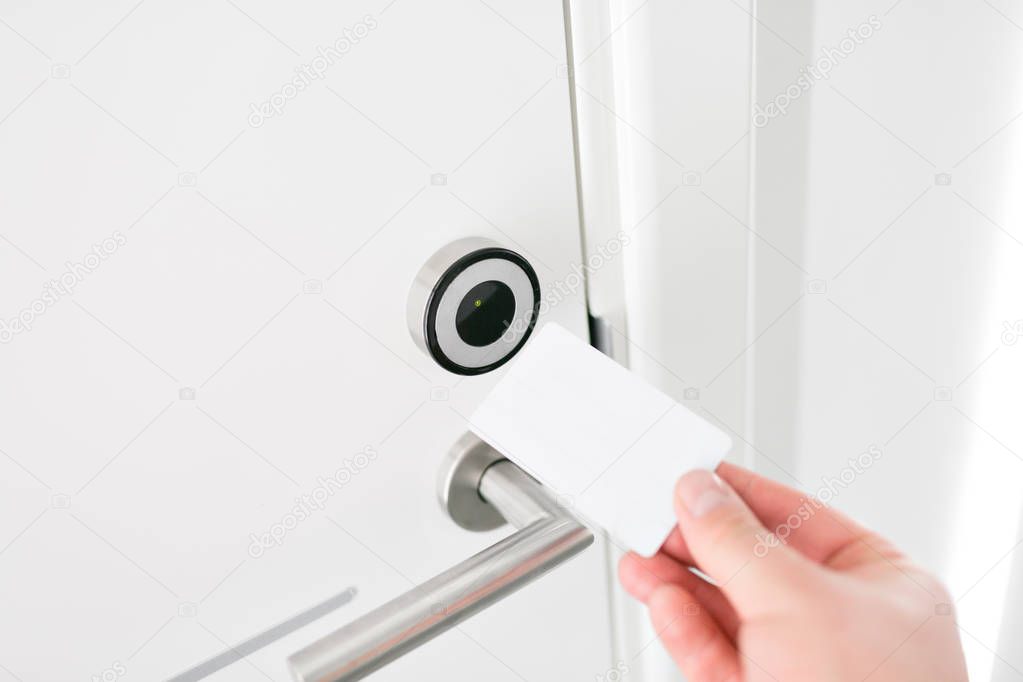 Hotel door - Young man holding a keycard in front of the electronic sensor of a room door. Concept travel or business trip