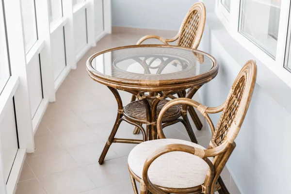 Mesa de cristal y silla de mimbre de ratán. Muebles de mimbre mesa de ratán dos sillas cerca de la ventana en el balcón — Foto de Stock