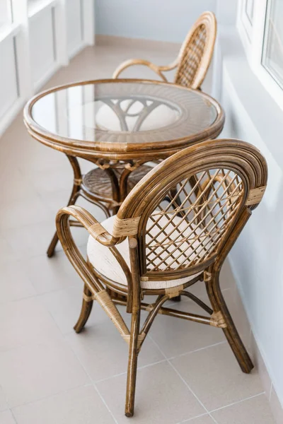 glass table and rattan wicker seat chair. Wicker furniture rattan table two chairs near the window on balcony