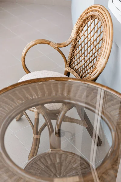 glass table and rattan wicker seat chair. Wicker furniture rattan table two chairs near the window on balcony