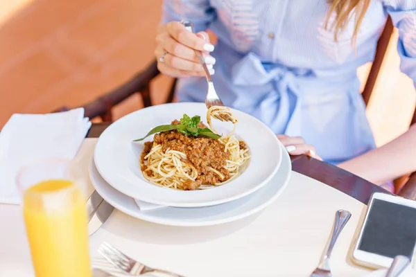 Young happy woman sitting at the table in cafe and enjoying the meal. Hungry woman eating tasty pasta. Dish of spaghetti Bolognese — Stock Photo, Image