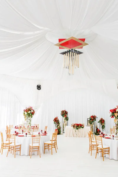 Beautiful banquet hall under a tent for a wedding reception. Interior of a wedding tent decoration ready for guests. Decor flowers. Red theme