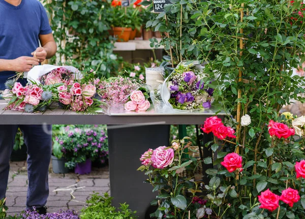 Male florist creating beautiful bouquet in flower shop. outdoor working in flower shop. Man assistant or owner in floral design studio, making decorations and arrangements.