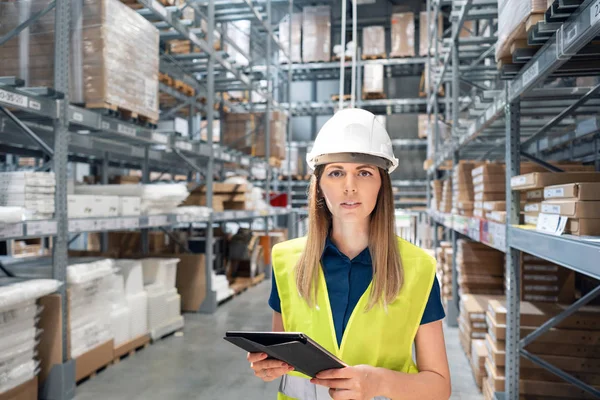 Beautiful young woman worker of furniture store in shopping center. Girl looking for goods with a tablet is checking inventory levels in a warehouse. Logistics concept
