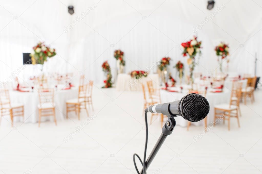 Microphone close-up. Focus on mic. Abstract blurred conference hall or wedding banquet on background. Event concept