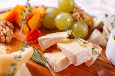 Peynir tabağı. Lezzetli peynir karışımı ile ceviz, bal, üzüm ahşap masa üzerinde. Ahşap bir tabakta yemek tatma. Yiyecek şarap.