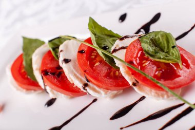 İtalyan Caprese salatası. Mozzarella peyniri, domates ve fesleğen bitki yaprakları. Beyaz tabakta düzenlenmiş balsamik sirke