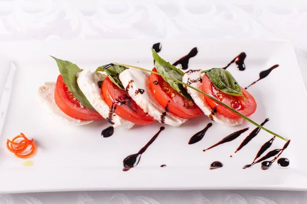 Salade italienne Caprese. Fromage mozzarella, tomates et feuilles de basilic. Vinaigre balsamique disposé sur une assiette blanche — Photo