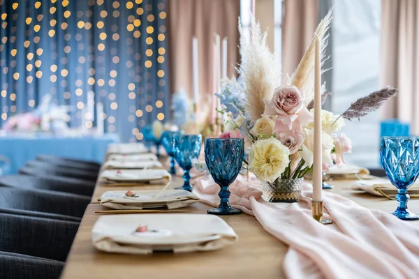 Mooie en verfijnde decoratie van het huwelijksfeest. Feestzaal geserveerd tafel met een beige roze tafelkleed, borden en kandelaars met kaarsen. — Stockfoto