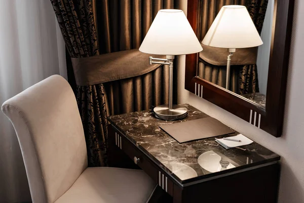 Apartamento interior del hotel, habitación cómoda, espejo y escritorio. carpeta para notas y lámpara de pie sobre una mesa en una habitación de hotel — Foto de Stock